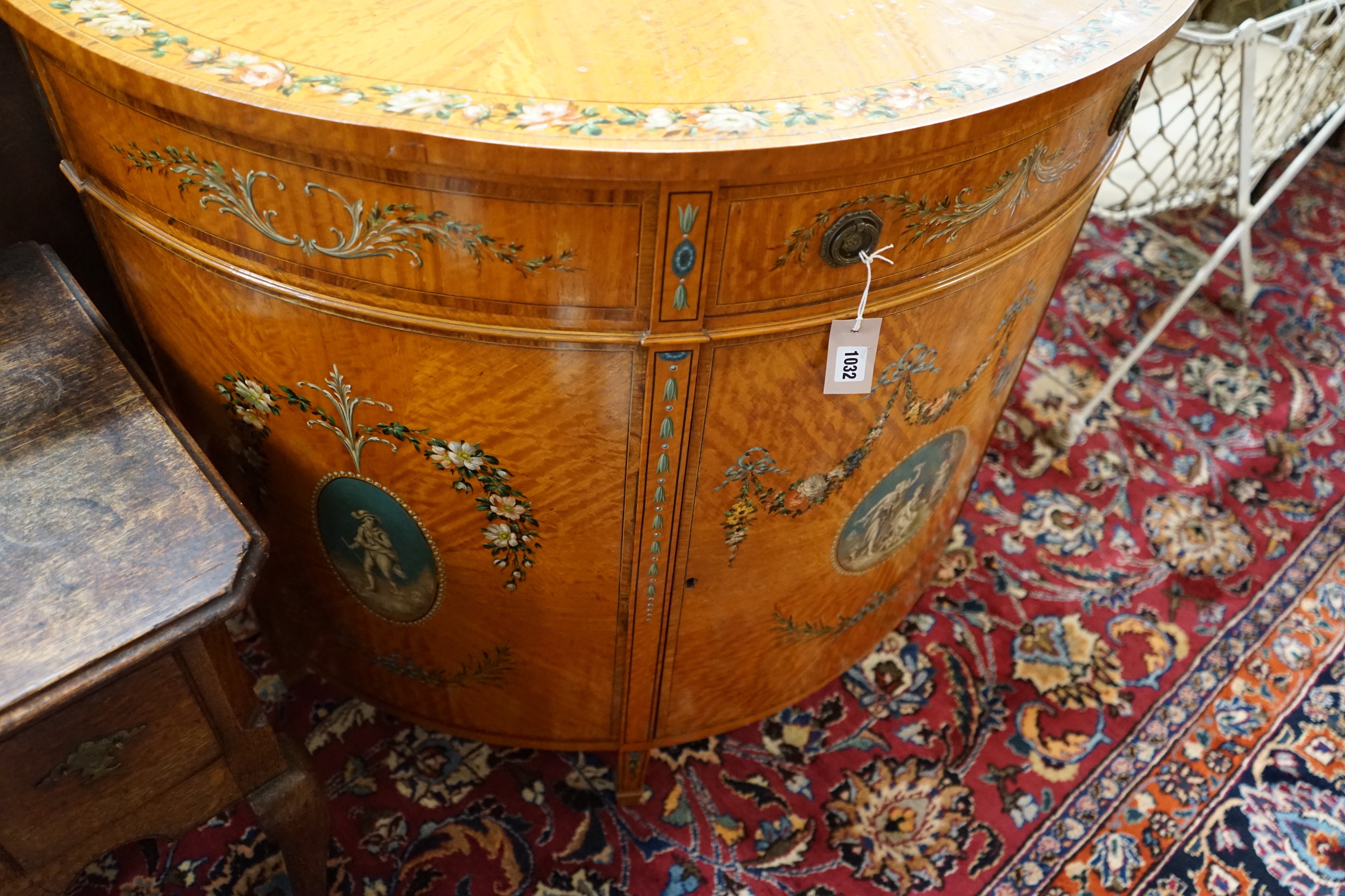 An Edwardian Sheraton revival painted satinwood demi lune side cabinet, width 107cm, depth 52cm, height 93cm